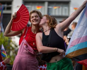 Young girl holding a flag and kissing a girl on her cheek with smiles during the canal pride 2024