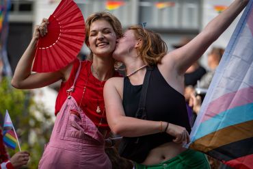 Young girl holding a flag and kissing a girl on her cheek with smiles during the canal pride 2024