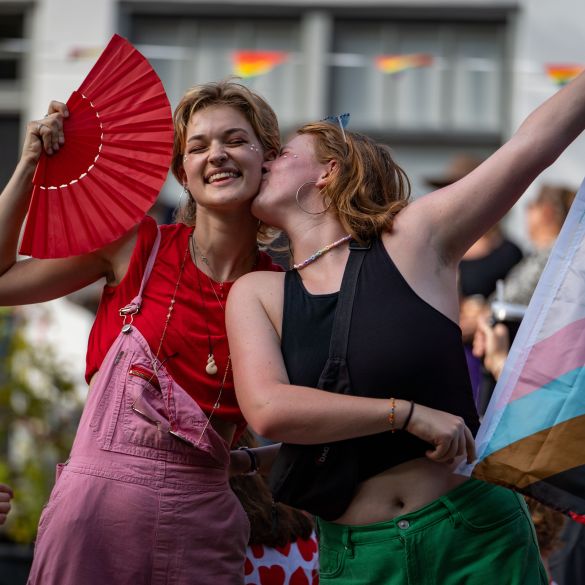 Young girl holding a flag and kissing a girl on her cheek with smiles during the canal pride 2024